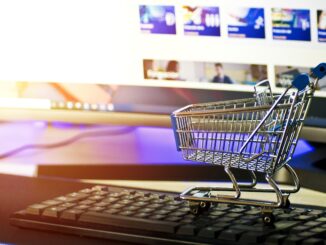 Miniatur-Einkaufswagen auf Tastatur, symbolisiert E-Commerce vor Computerbildschirm.