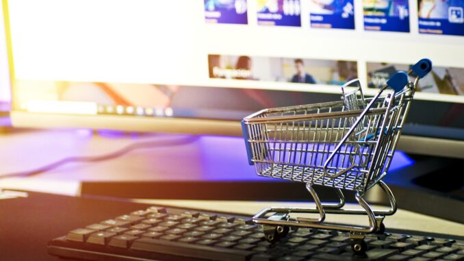 Miniatur-Einkaufswagen auf Tastatur, symbolisiert E-Commerce vor Computerbildschirm.
